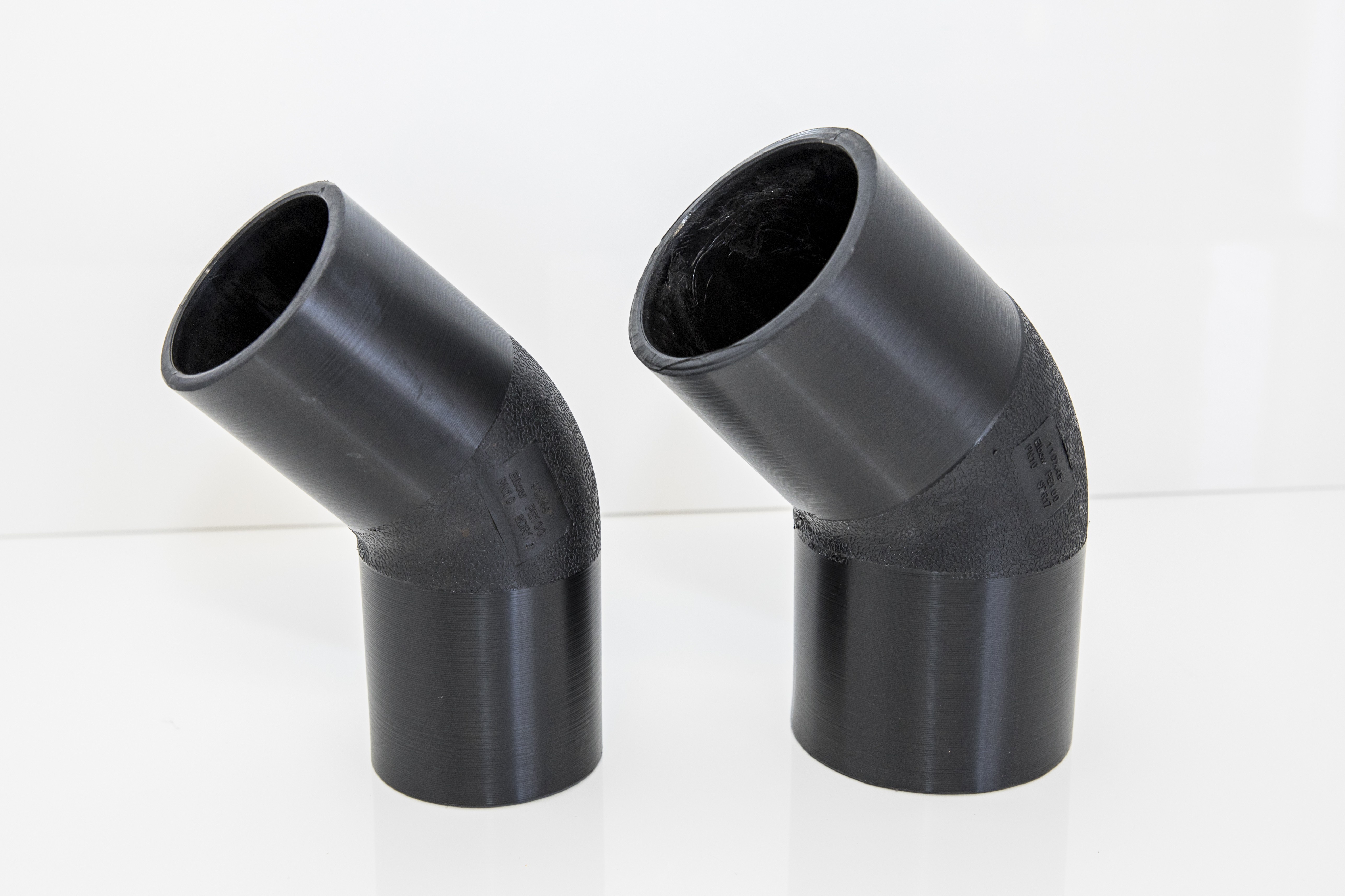 An image of two 45 degree polyethylene elbows standing next to each other against a white background.